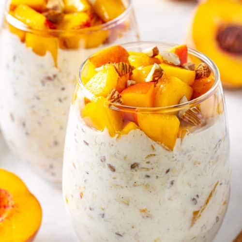 peach overnight oats on a marble surface with almond chunks and slices of peaches on top of the oats