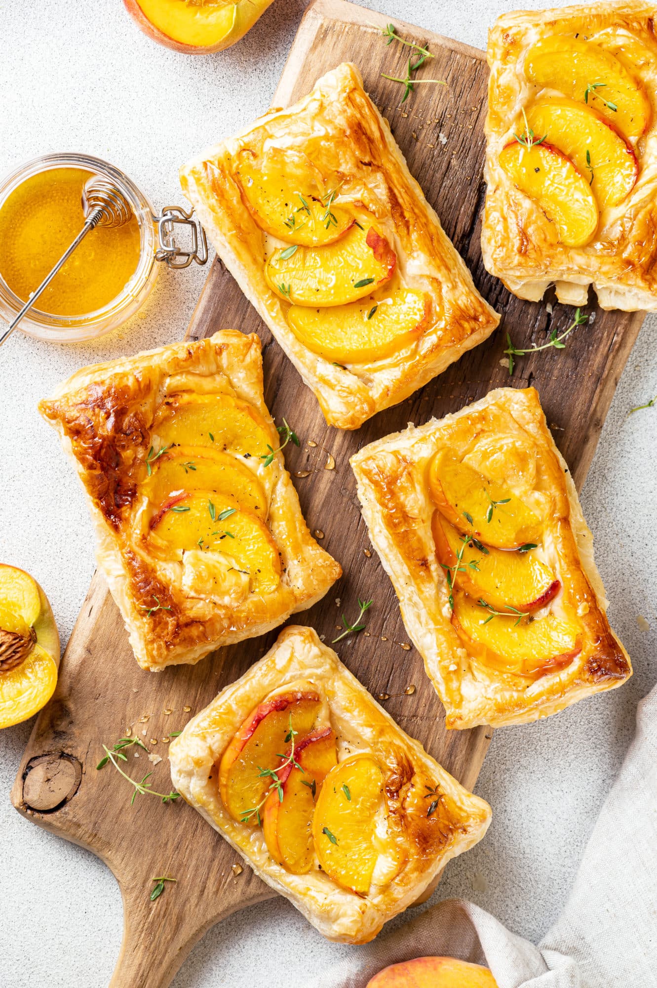 A wooden board with baked peach and brie tarts with honey on the side.