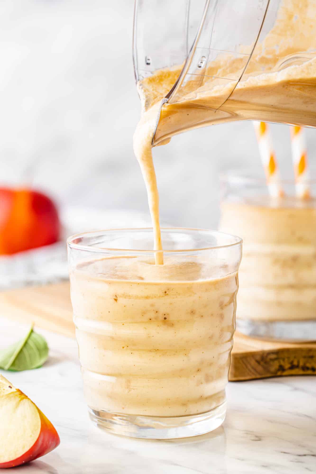 Apple smoothie in a cup with a blender pouring more smoothie into the cup.