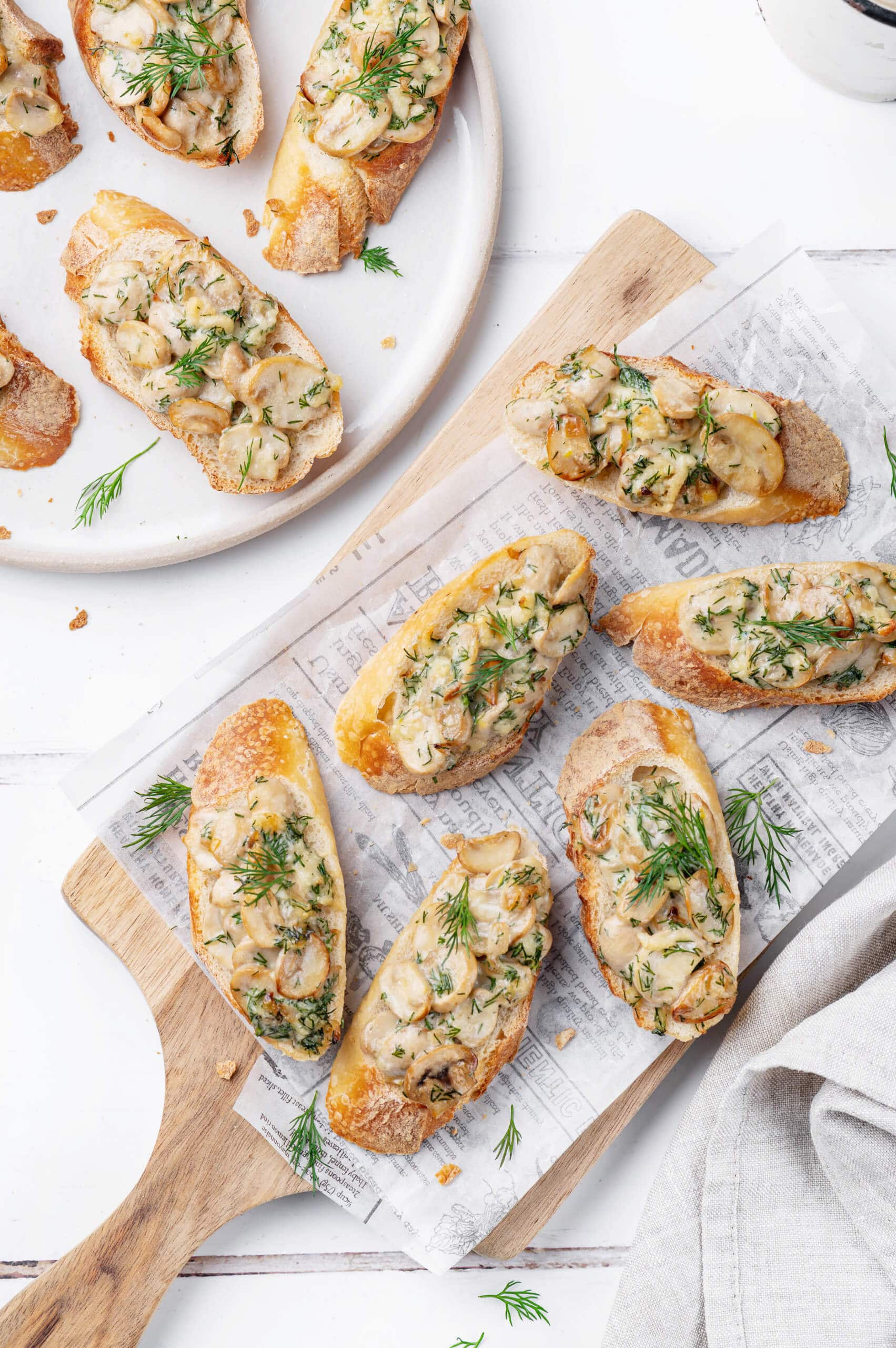 mushroom-crostini-on-wooden-cutting-board-with-paper-and-crostinis-on-white-plate