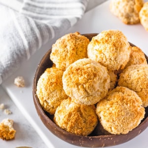 Macaroons in a wooden bowl on a white board.