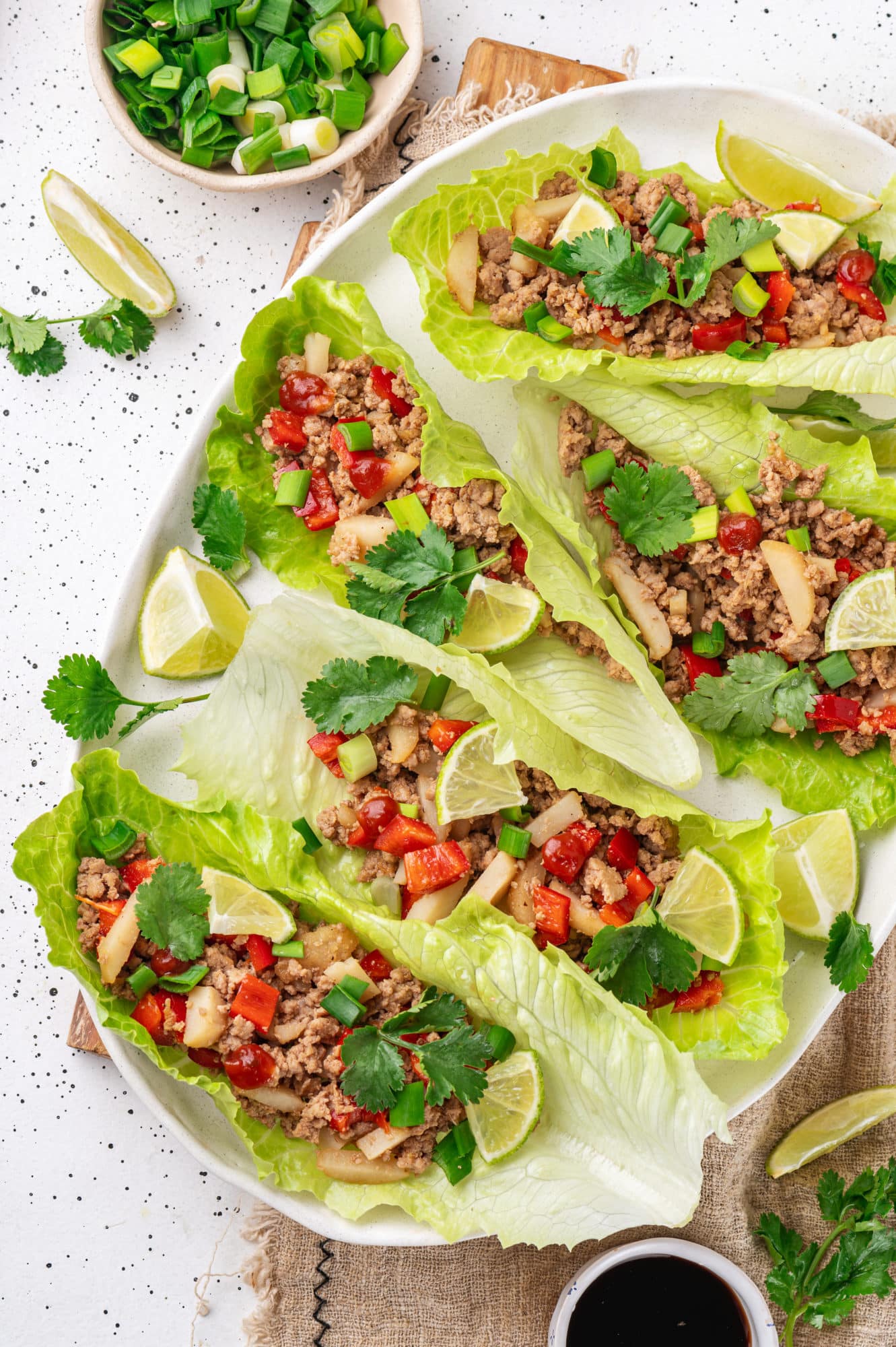 Turkey lettuce wraps on a white plate with a linen towel underneath and scallions chopped in a small bowl on the side.