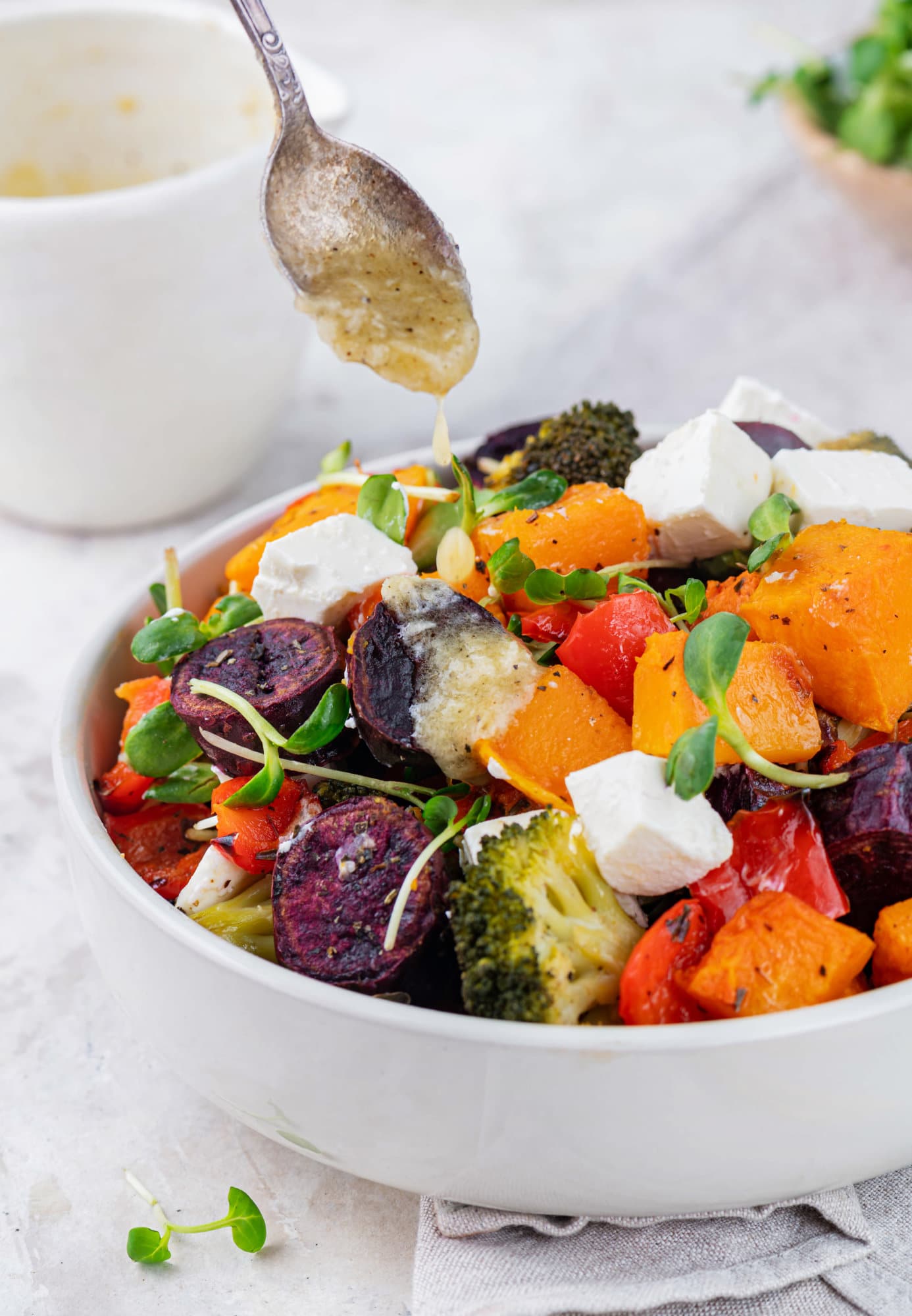 a spoon drizzling dressing atop roasted veggies with fresh microgreens on top.