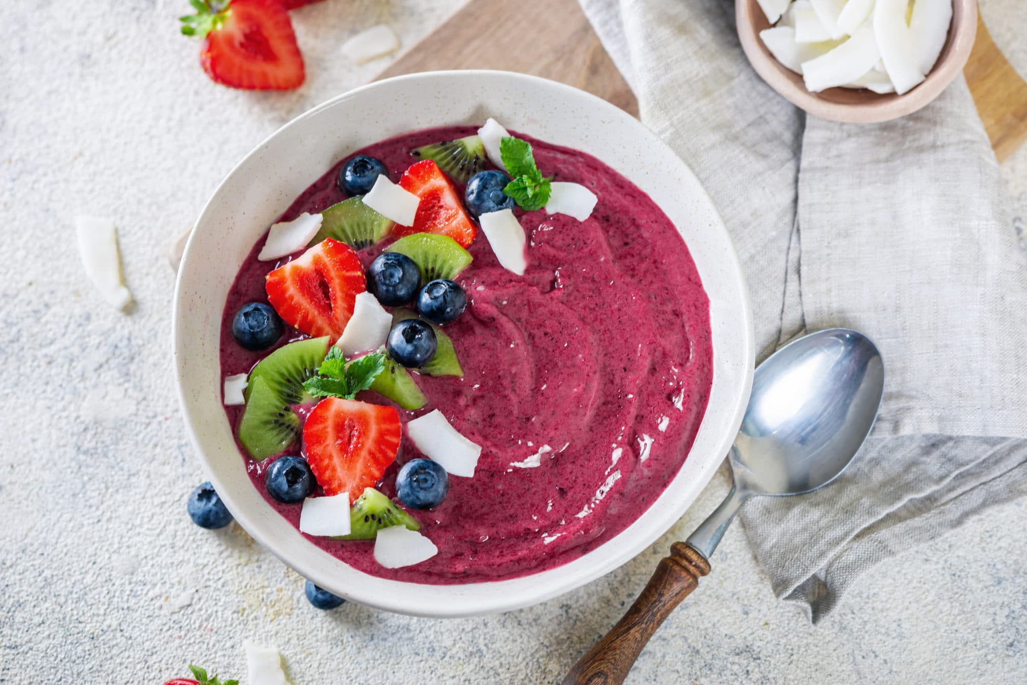 Acai smoothie in a white bowl with toppings and a spoon on the side. 