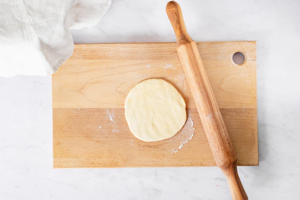 A circle of dough rolled out on a wooden cutting board with a rolling pin.