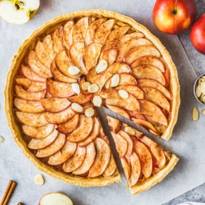 apple tart on parchment paper with one slice cut.