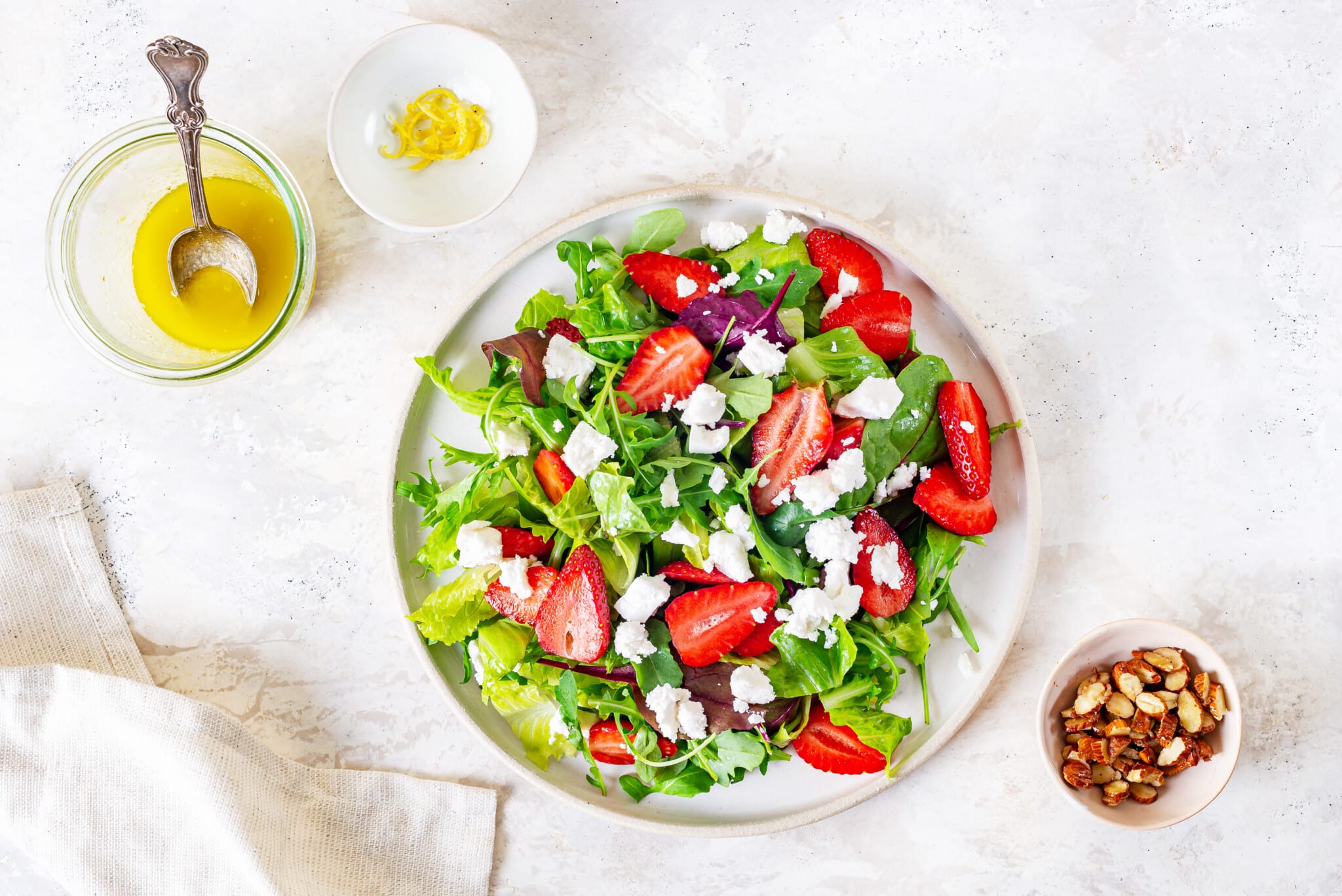 greens on a white plate with chopped strawberries and goat cheese on top with dressing on the side.