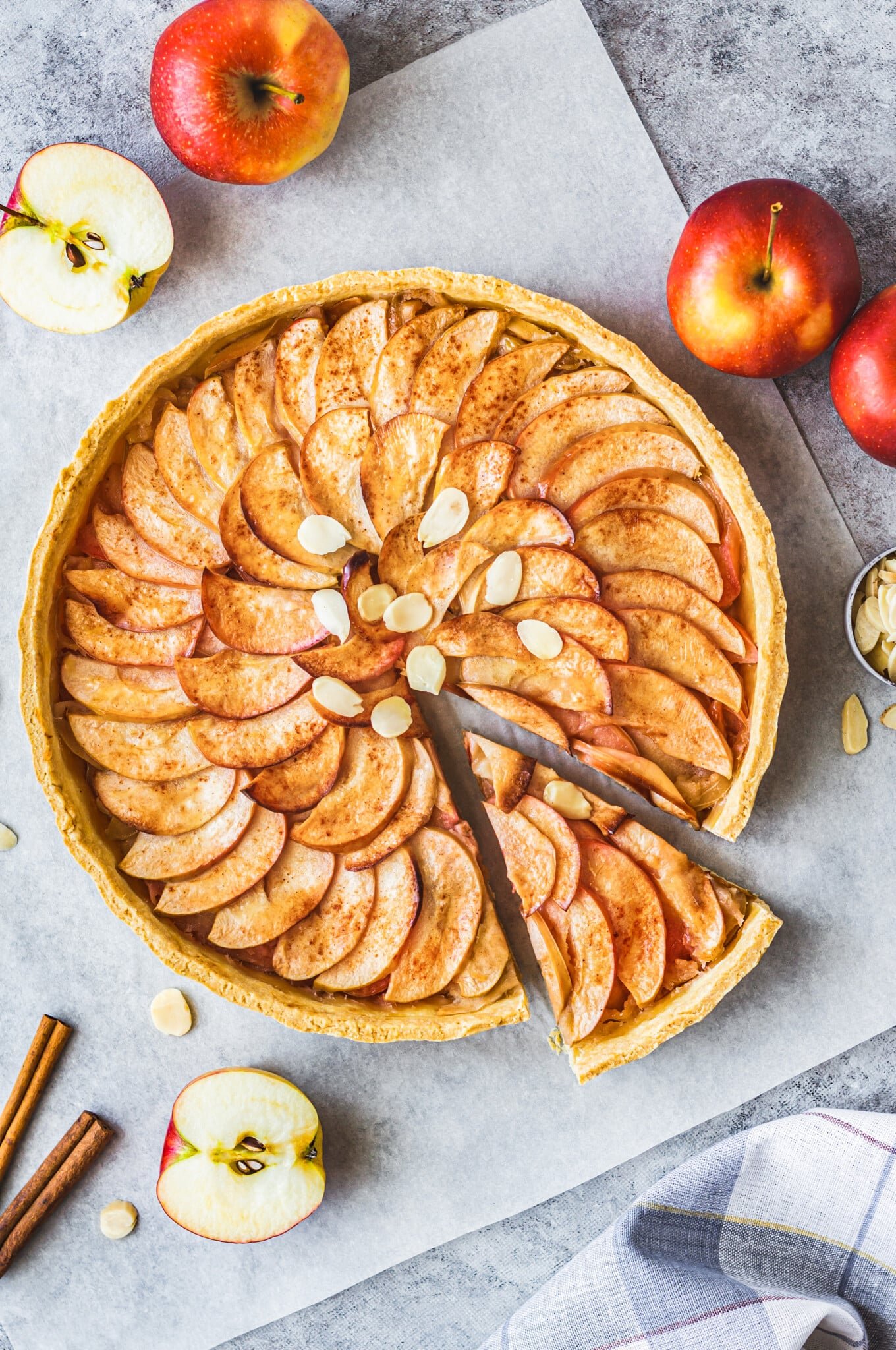 apple tart on parchment paper with one slice cut.