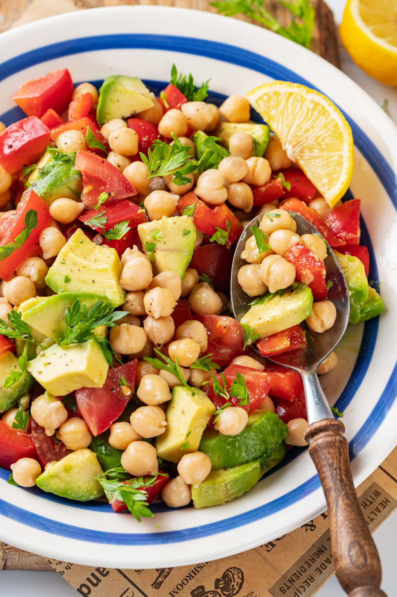 Chickpea avocado salad in a blue striped bowl with parsley sprinkled throughout, and a spoon on the side.