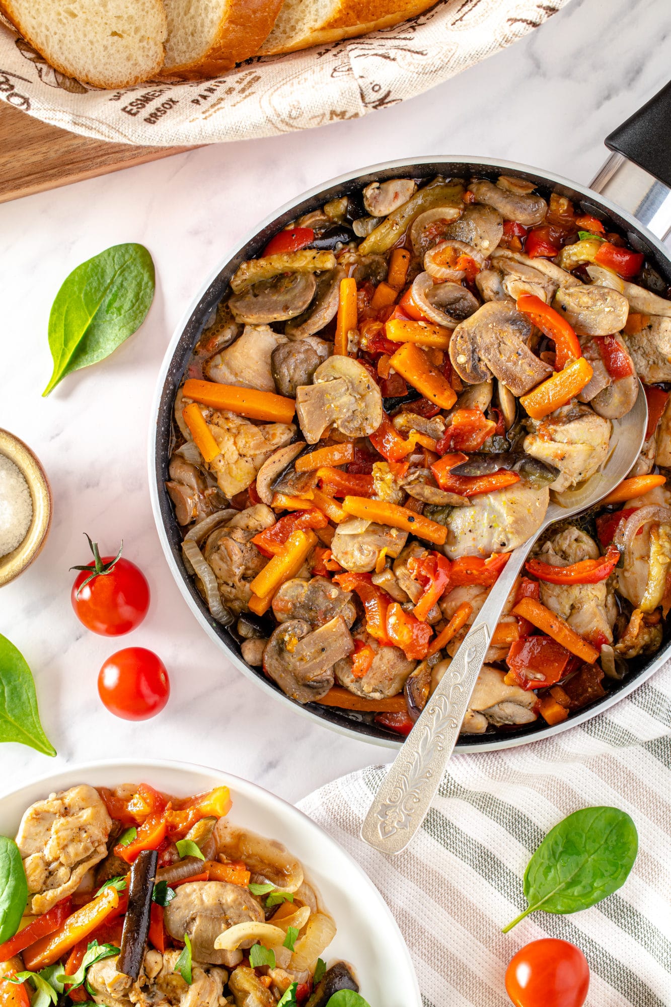 black-skillet-pan-with-skinless-boneless-chicken-thighs-with-olive-oil-sliced-carrots-on-white-surface-cherry-tomatoes-basil-leaves-slices-of-bread