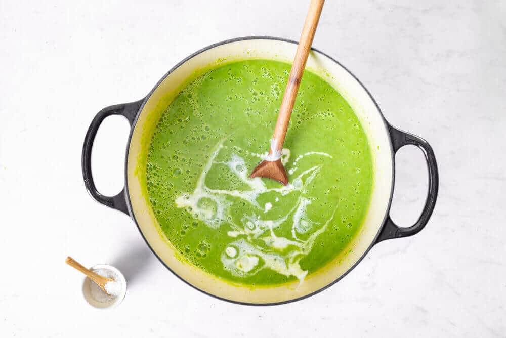 blended pea soup in a large soup pot with cream added on top in swirls.