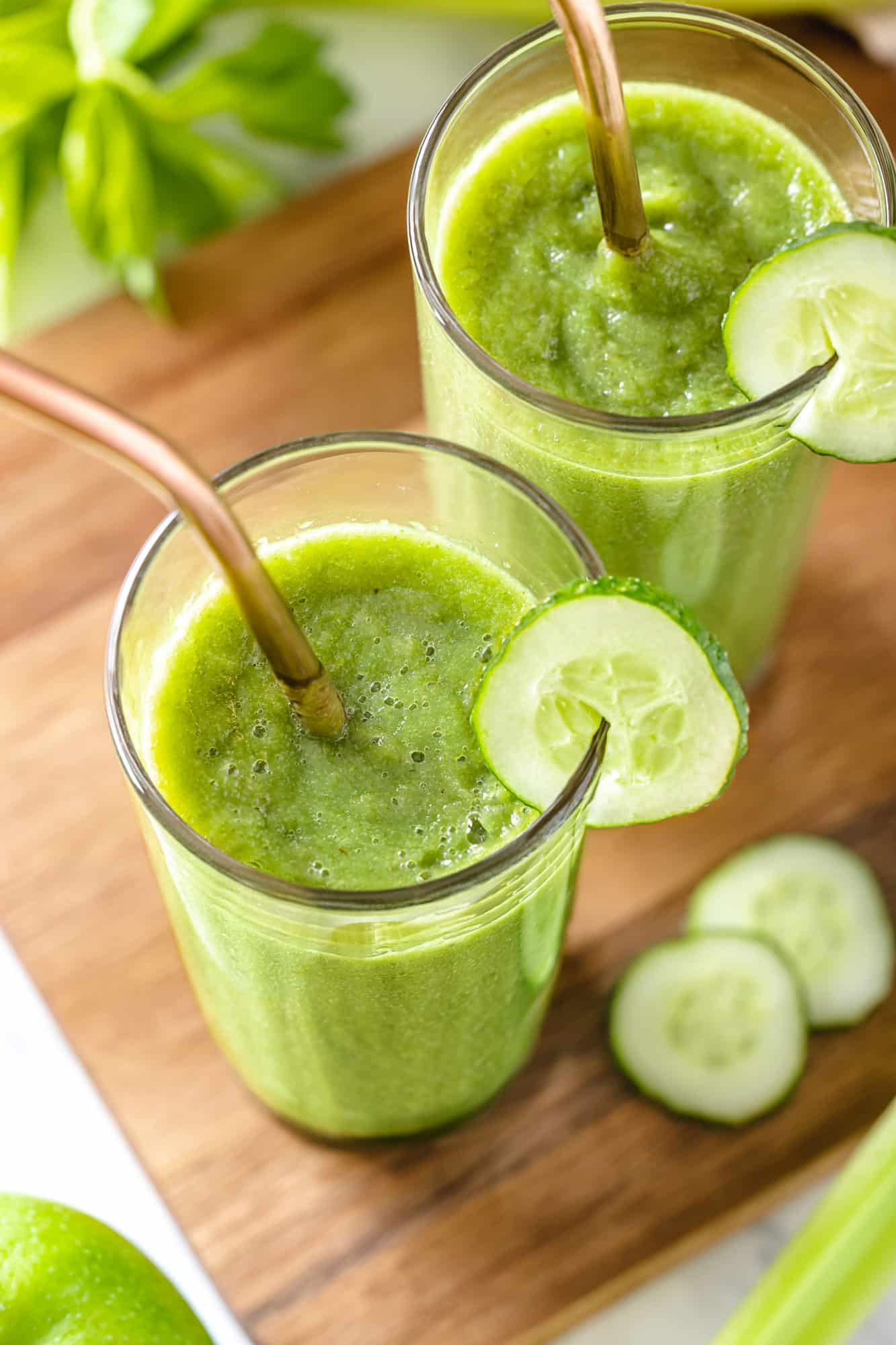 a wooden board with a blended green smoothie in glasses with straws.