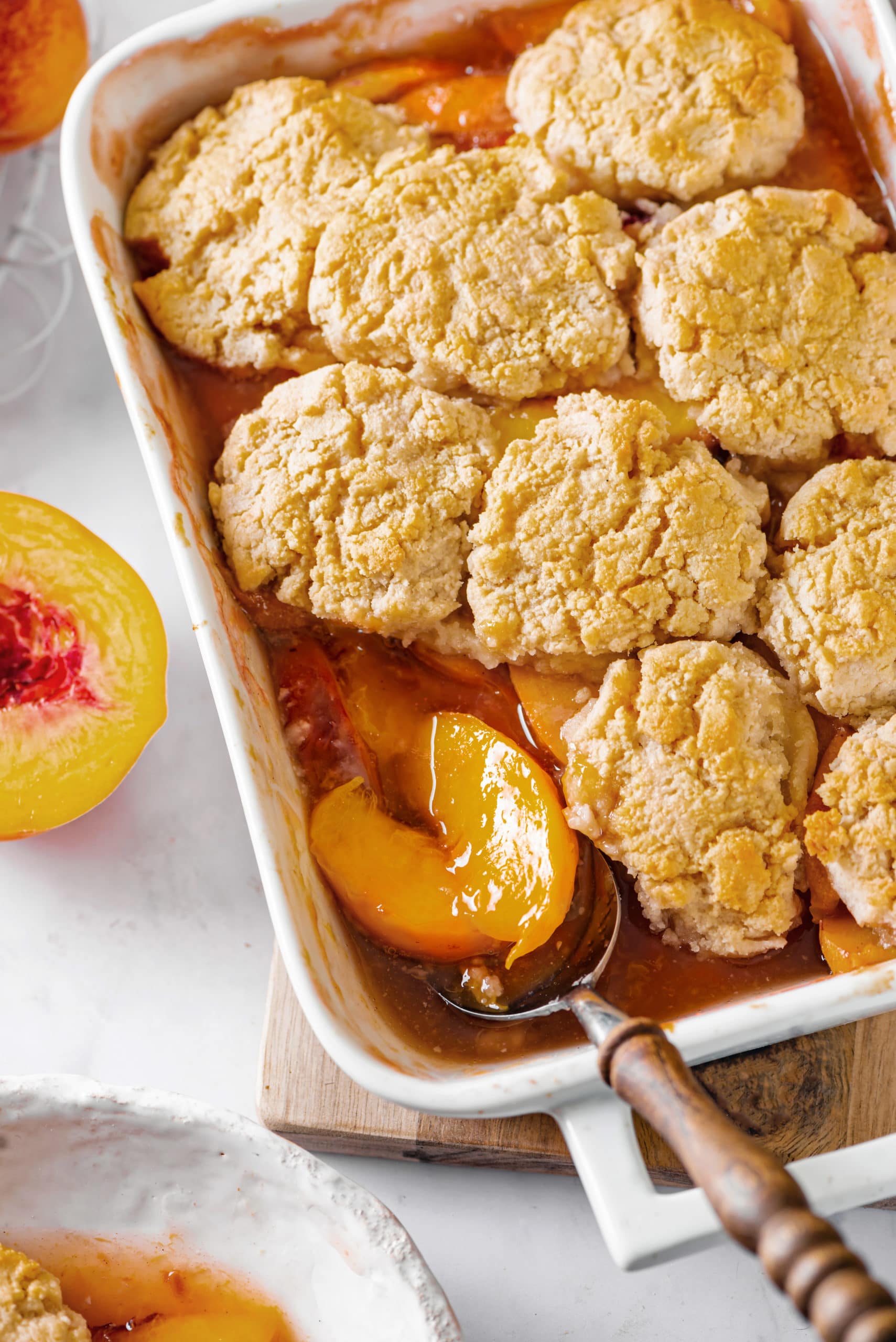 Peach cobbler in a baking tray, scooping peaches out.