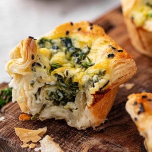 spinach puff close up on a wooden board with crumbs around.