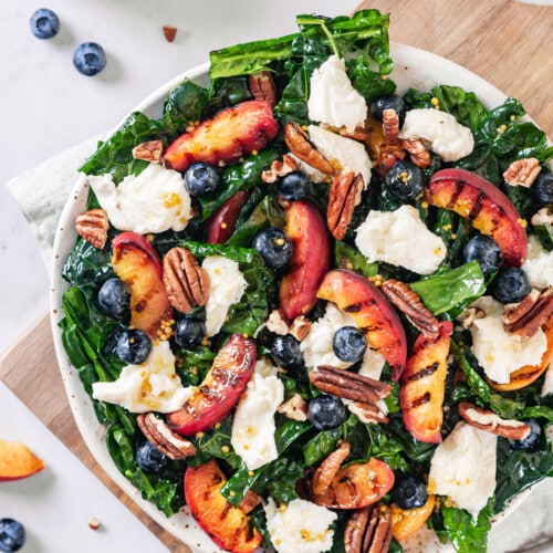 Peaches grilled and mixed with cheese, blueberries, and walnuts in a kale salad with a white bowl.