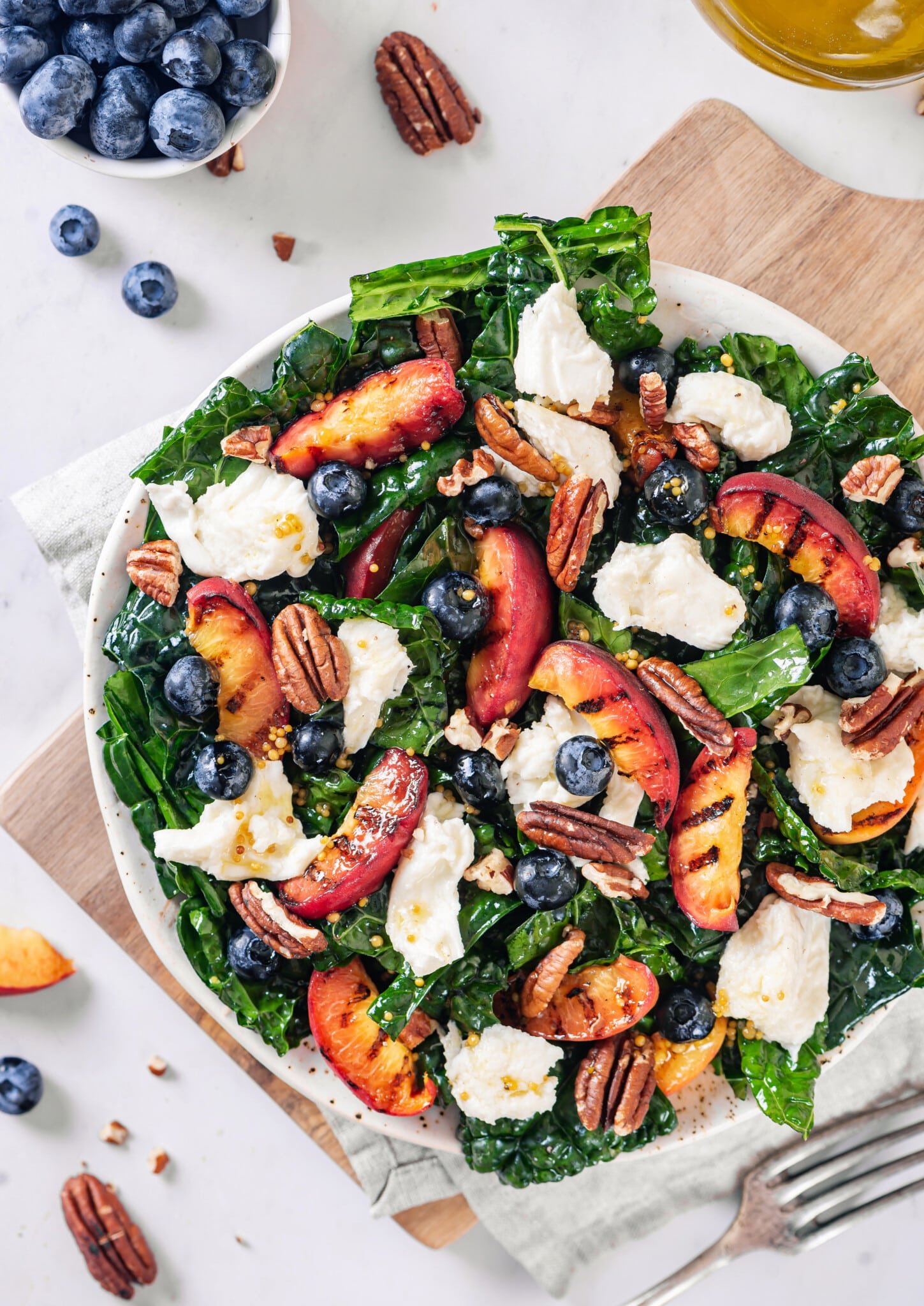 Peaches grilled and mixed with cheese, blueberries, and walnuts in a kale salad with a white bowl.