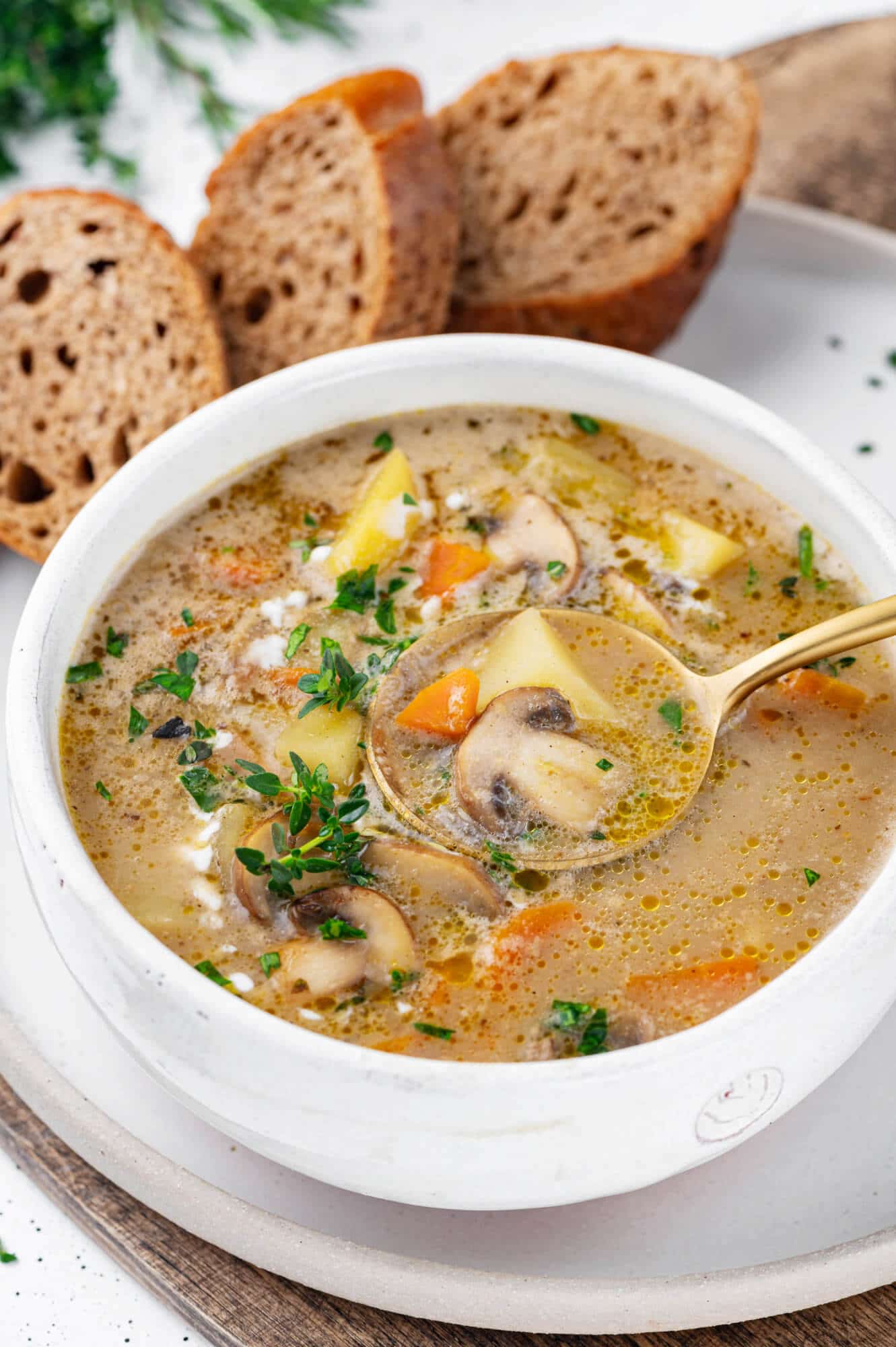 A white bowl filled with mushroom soup with mushrooms on top and a spoon in the bowl.