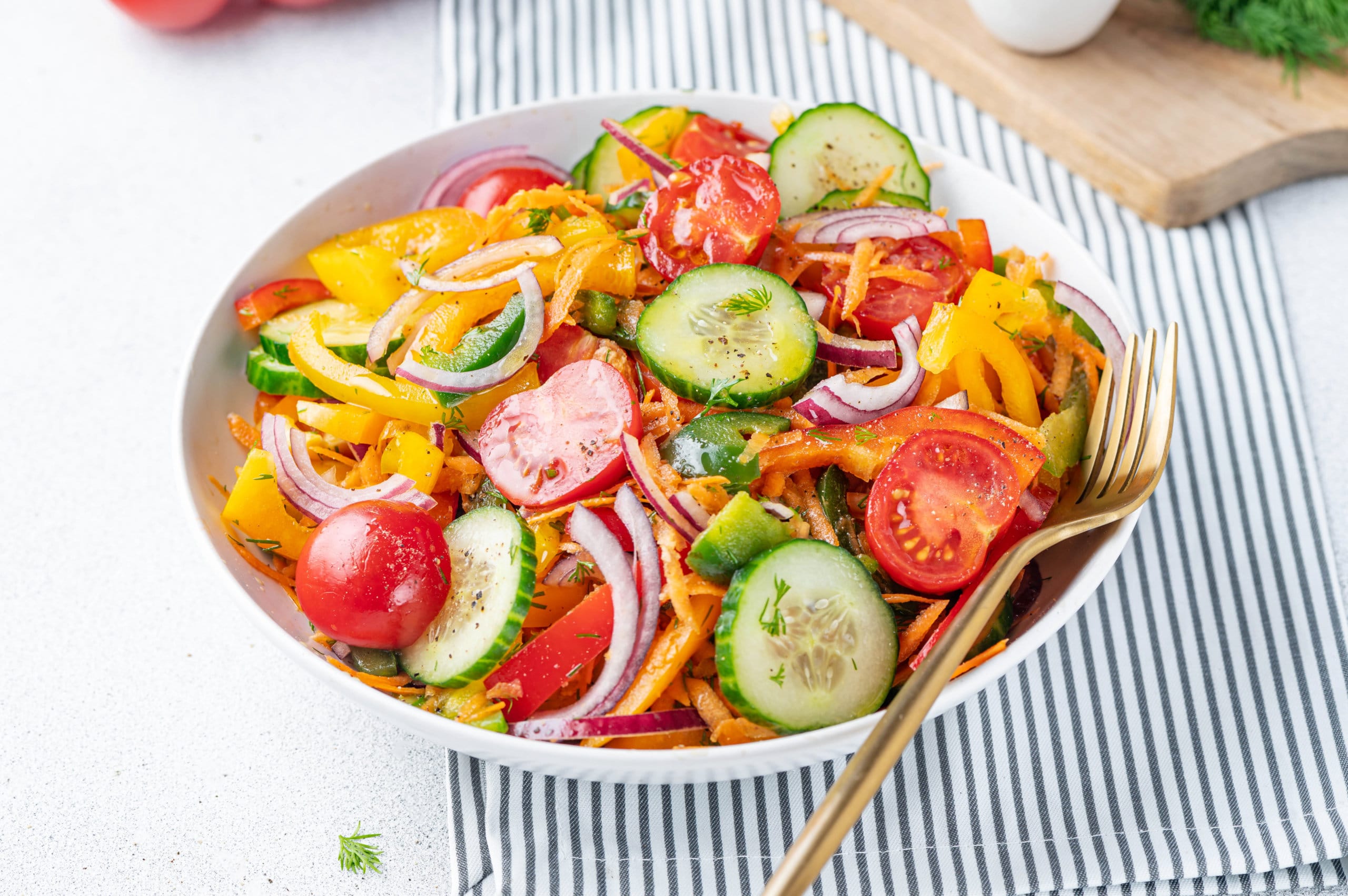 Low carb clean eating veggie bowl salad in a white bowl with a towel and a gold fork.