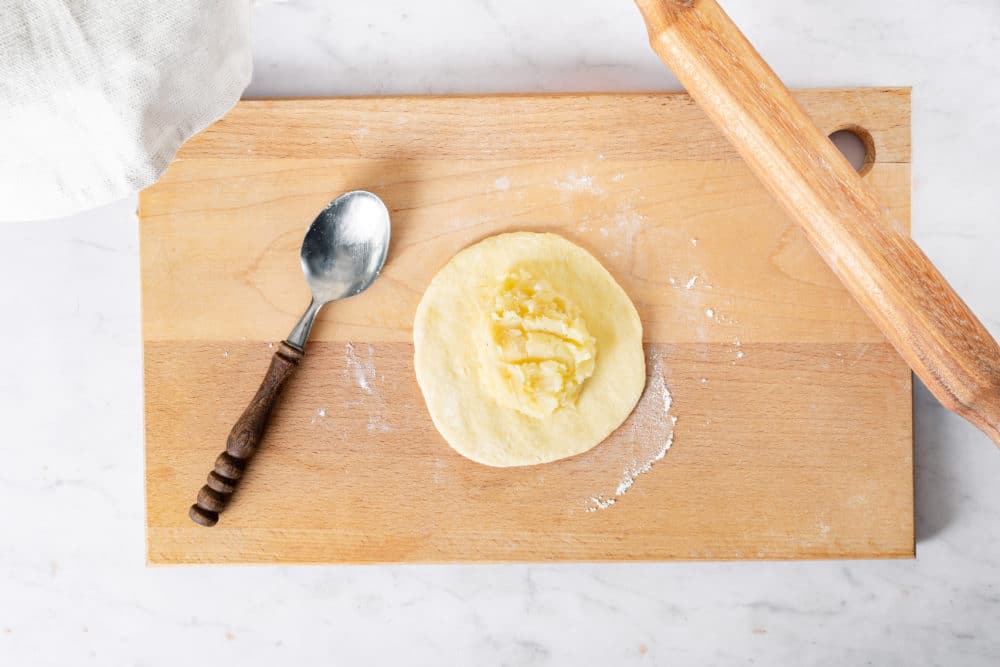 Rolled dough on a cutting board with mashed potato filling and a spoon on the side.