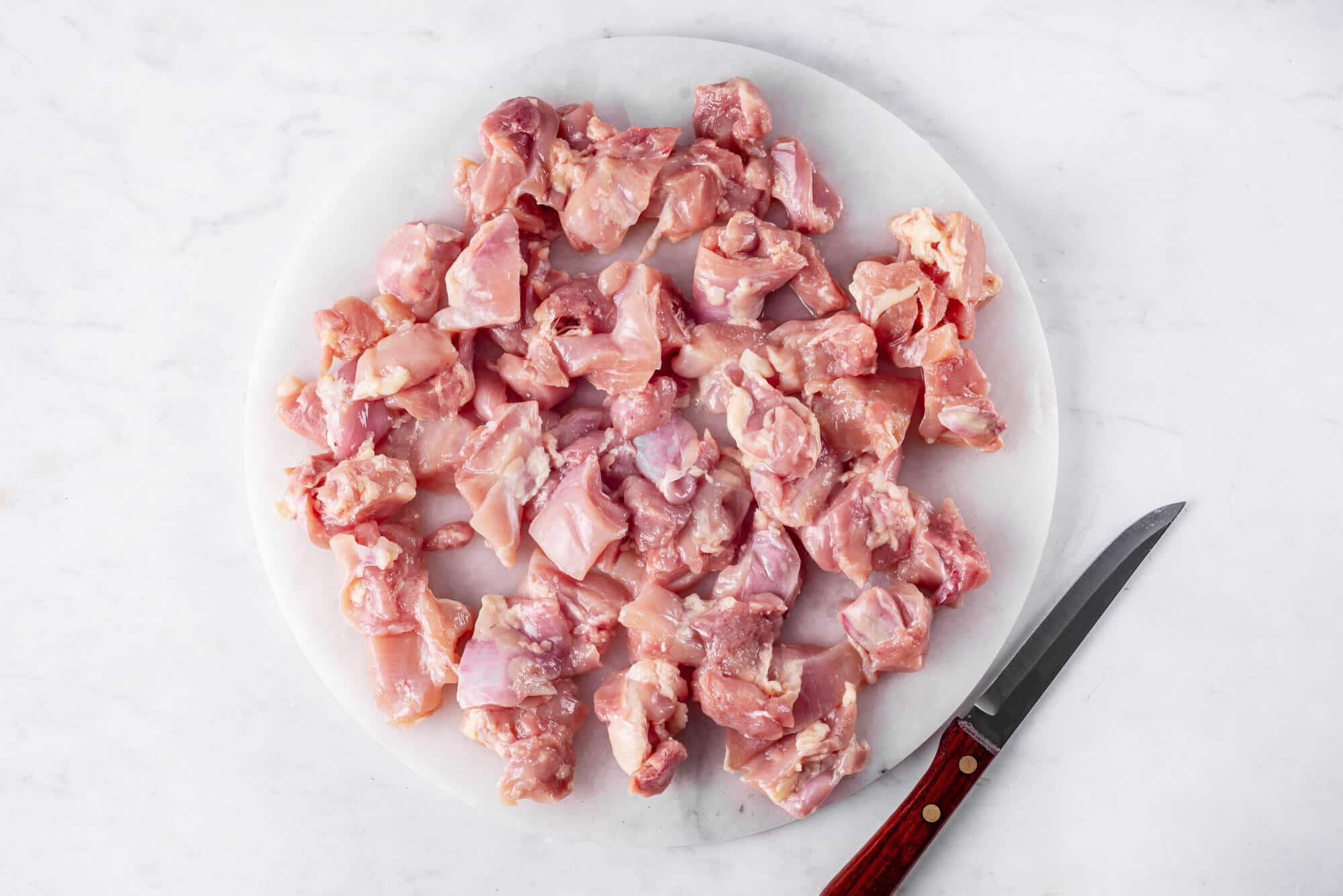 Cut raw chicken on a cutting board with a knife on the side.