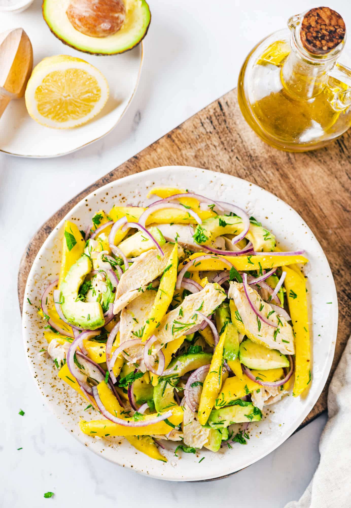 avocado-chicken-mango-salad-on-a-white-plate-on-a-wooden-board-with-olive-oil-and-a-lemon-wedge-on-the-side