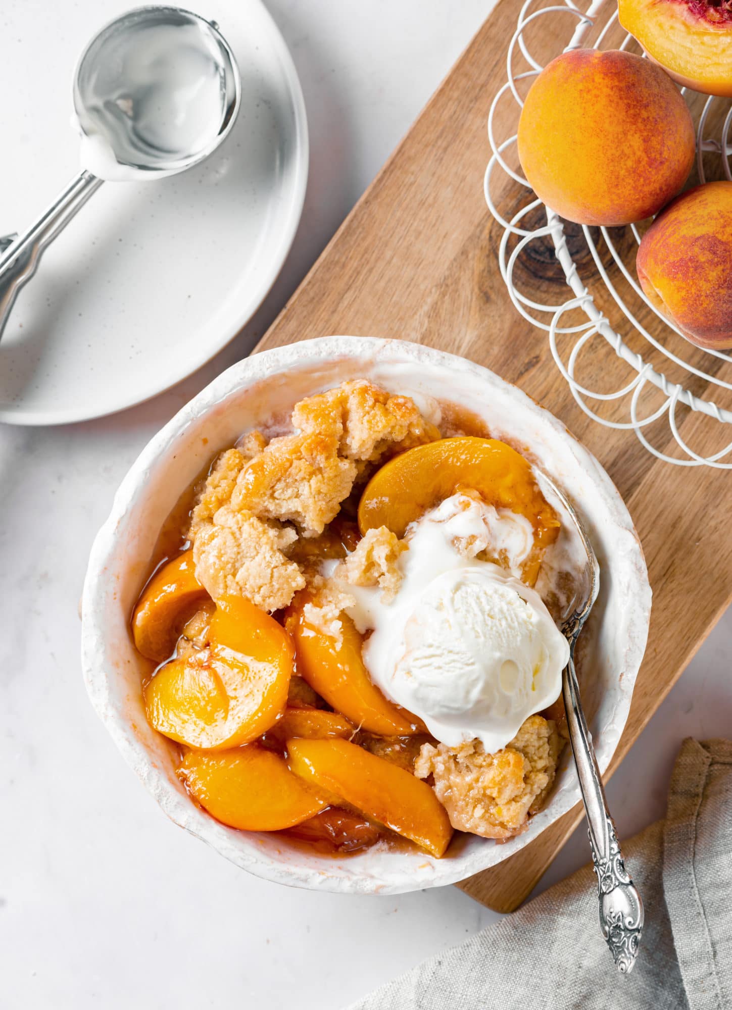 Fresh baked cobbler in a white dish with icecream on top.