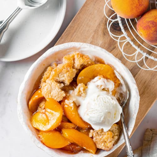 Fresh baked cobbler in a white dish with icecream on top.