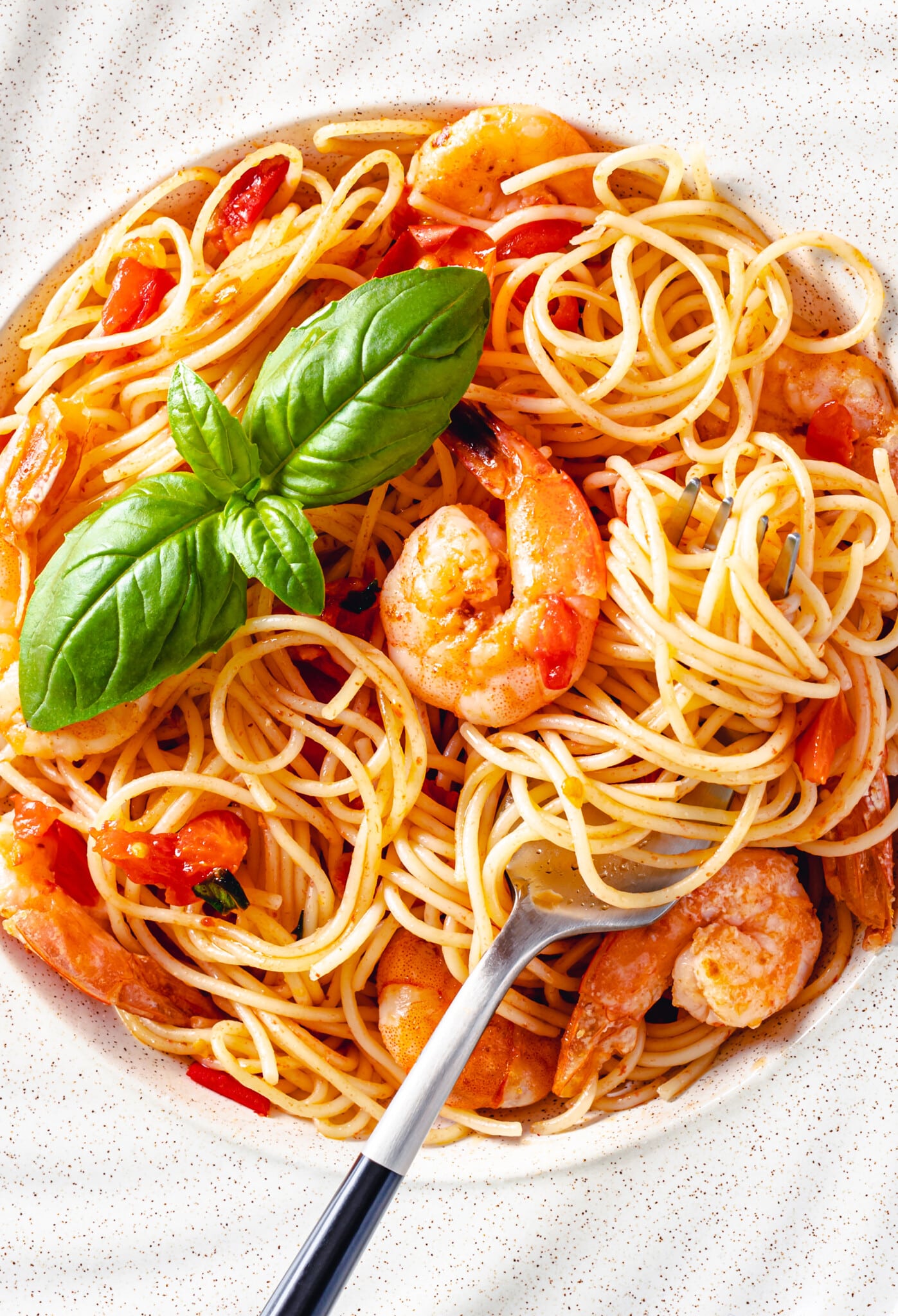 a white bowl filled with shrimp tomato pasta with basil on top and a fork.