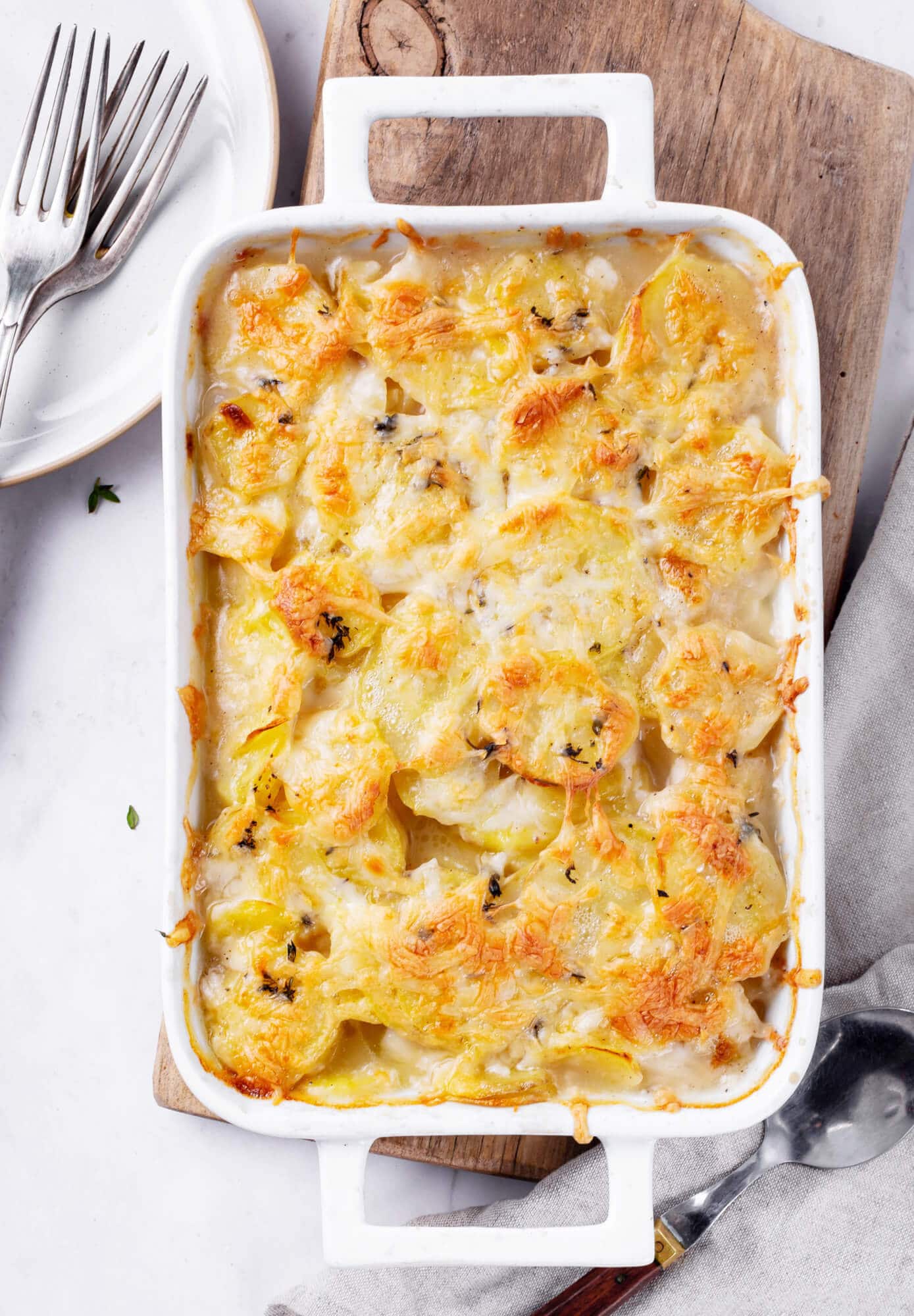 scalloped-potatoes-in-baking-dish-on-wooden-board-with-forks-on-the-side.