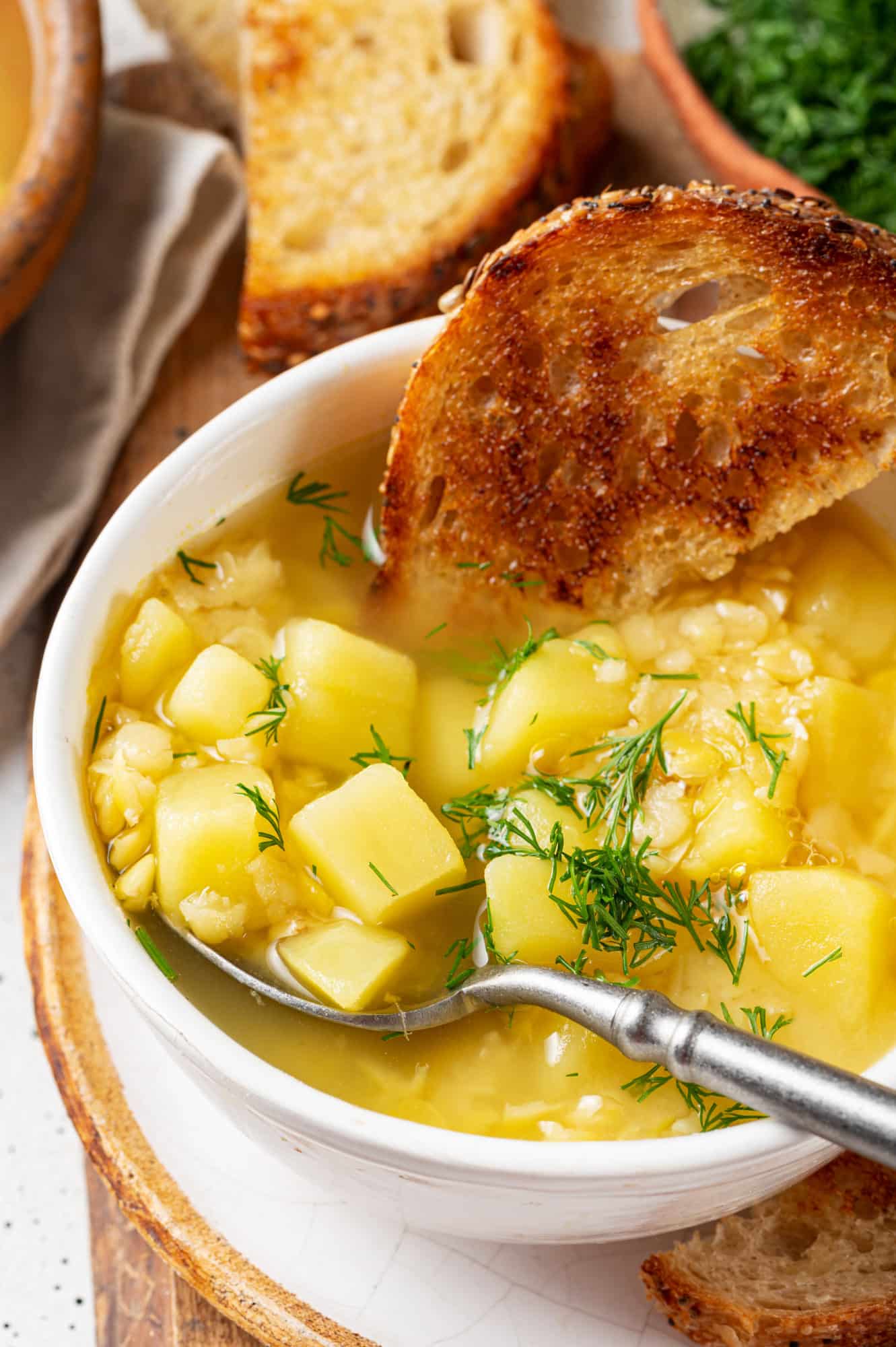 split pea soup with potatoes and toast in a white bowl and a silver soup. 