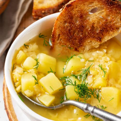 split-pea-soup-in-a-white-bowl-with-a-spoon-in-it-and-toast-slices-all-on-a-wooden-board