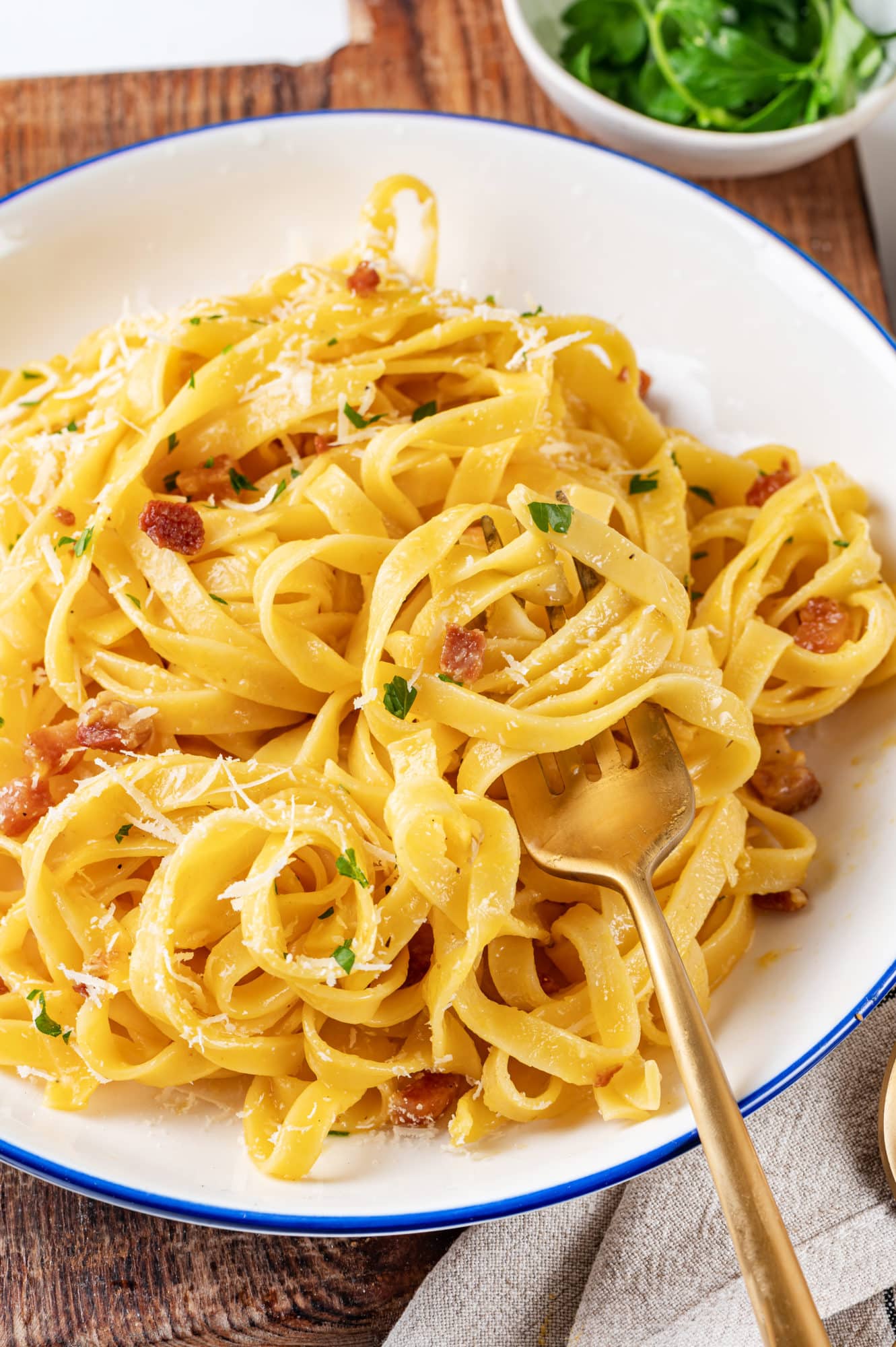 Pasta carbonara in a white bowl with a gold fork.