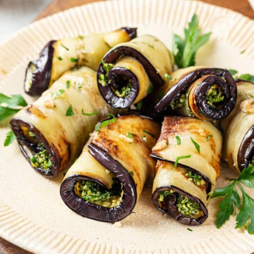 a beige plate with herb filled eggplant rolls with parsley.