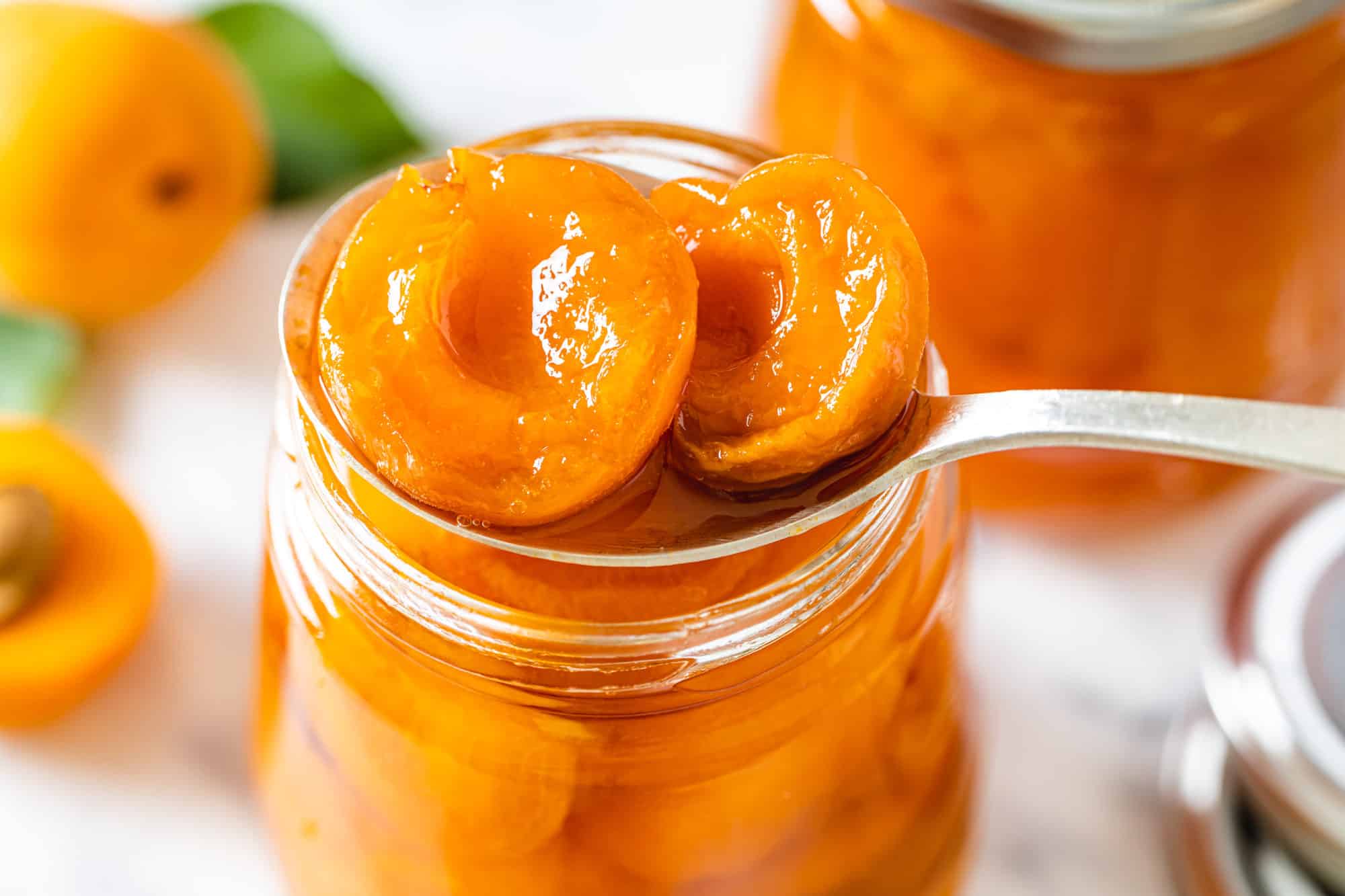 Closeup of a glass jar with apricots in a spoon.