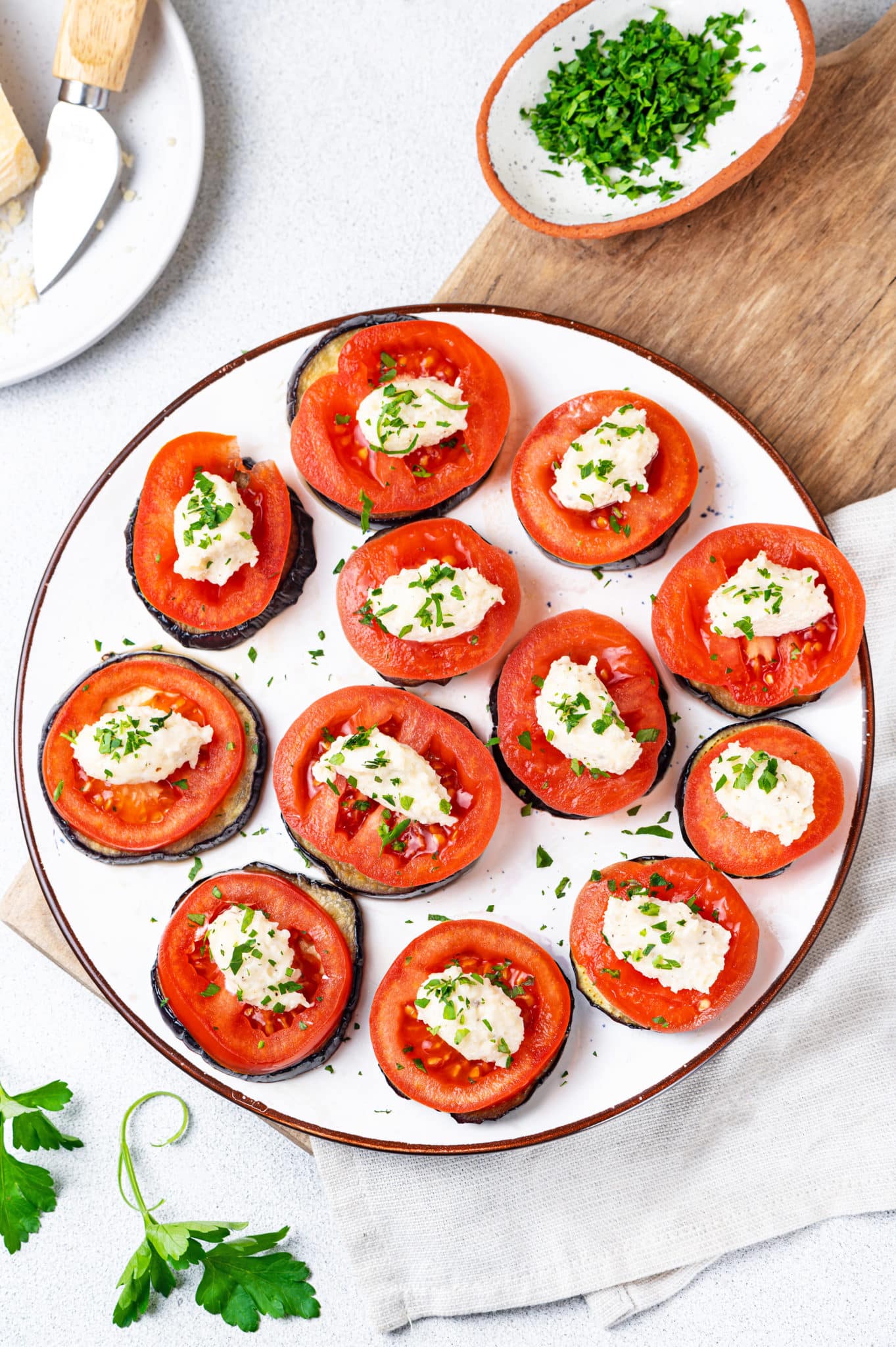 eggplant tomato appetizers on a white plate on a wooden board with a grey towel and extra herb topping on the side.