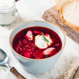 A bowl of borscht with a dollop of sour cream on top with a spoon on the side.