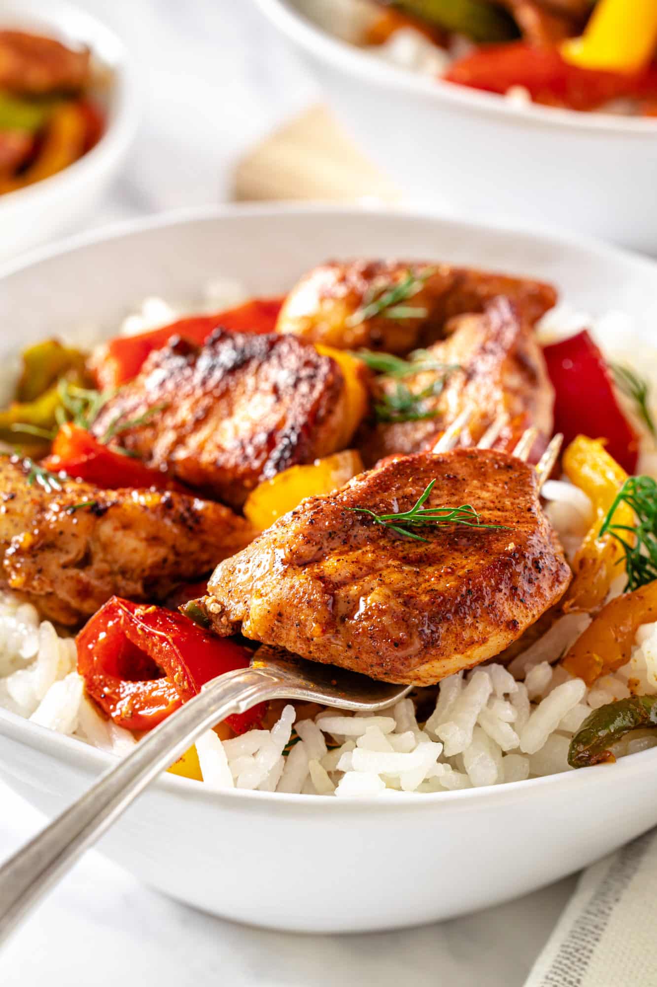 a white bowl with rice and sauteed chicken and bell peppers on top.