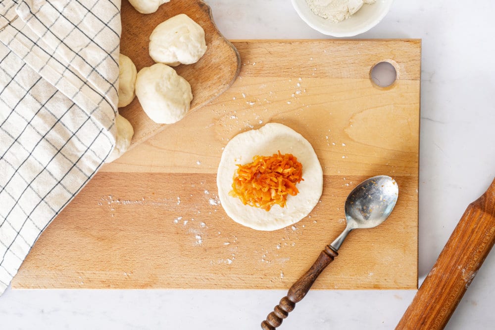 dough-round-with-cabbage-in-the-center-on-a-wooden-board-with-a-spoon-on-the-side-with-another-woode-board-with-dough-rounds-on-it-covered-by-a-towel