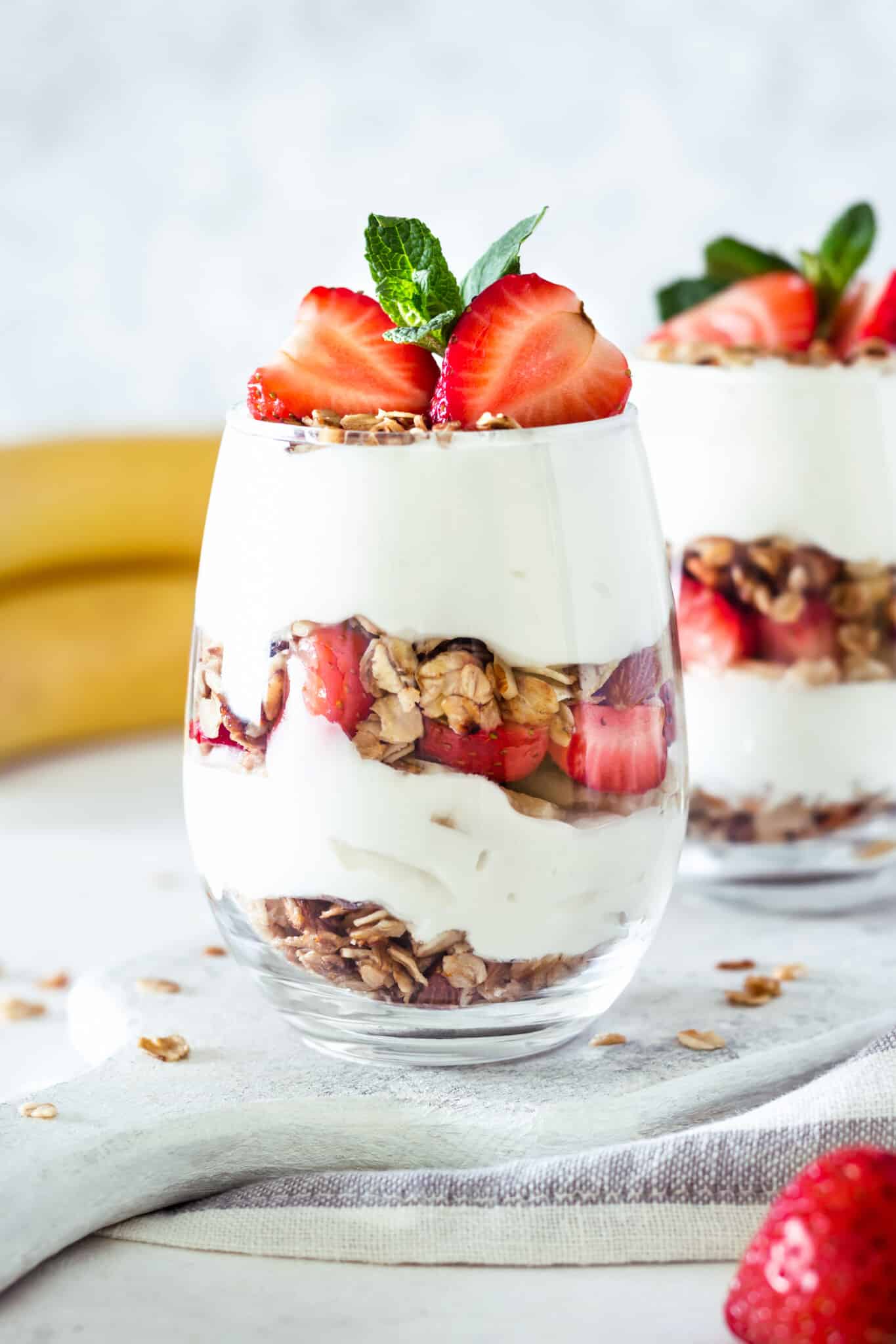 Granola yogurt breakfast parfait in a glass cup topped with fresh strawberries and mint.