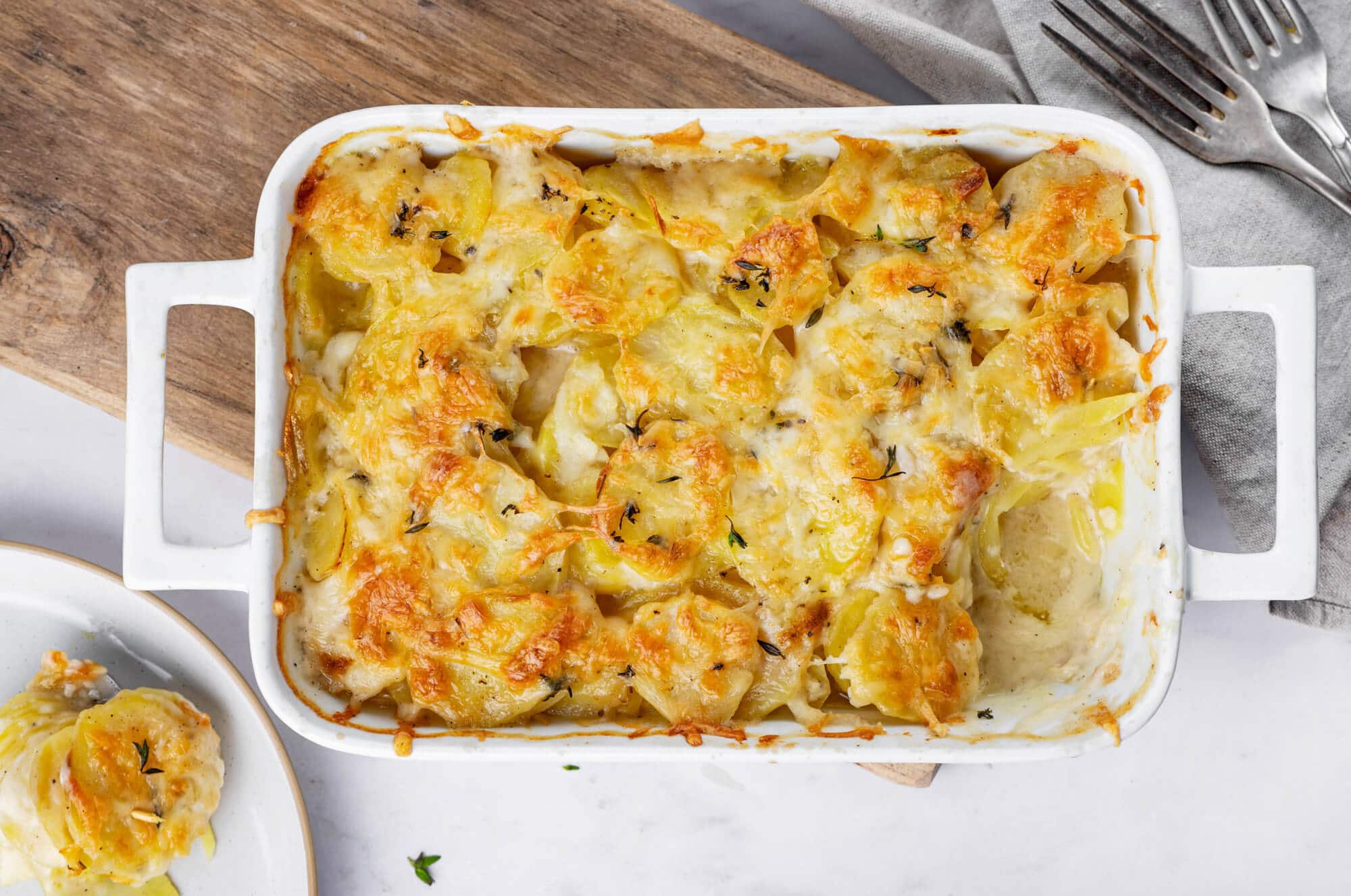 scalloped-potatoes-in-baking-dish-on-wooden-board-with-forks-on-the-side