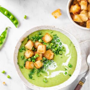 a bowl of pea soup with croutons on top and peas and a separate bowl of corutons on the side.