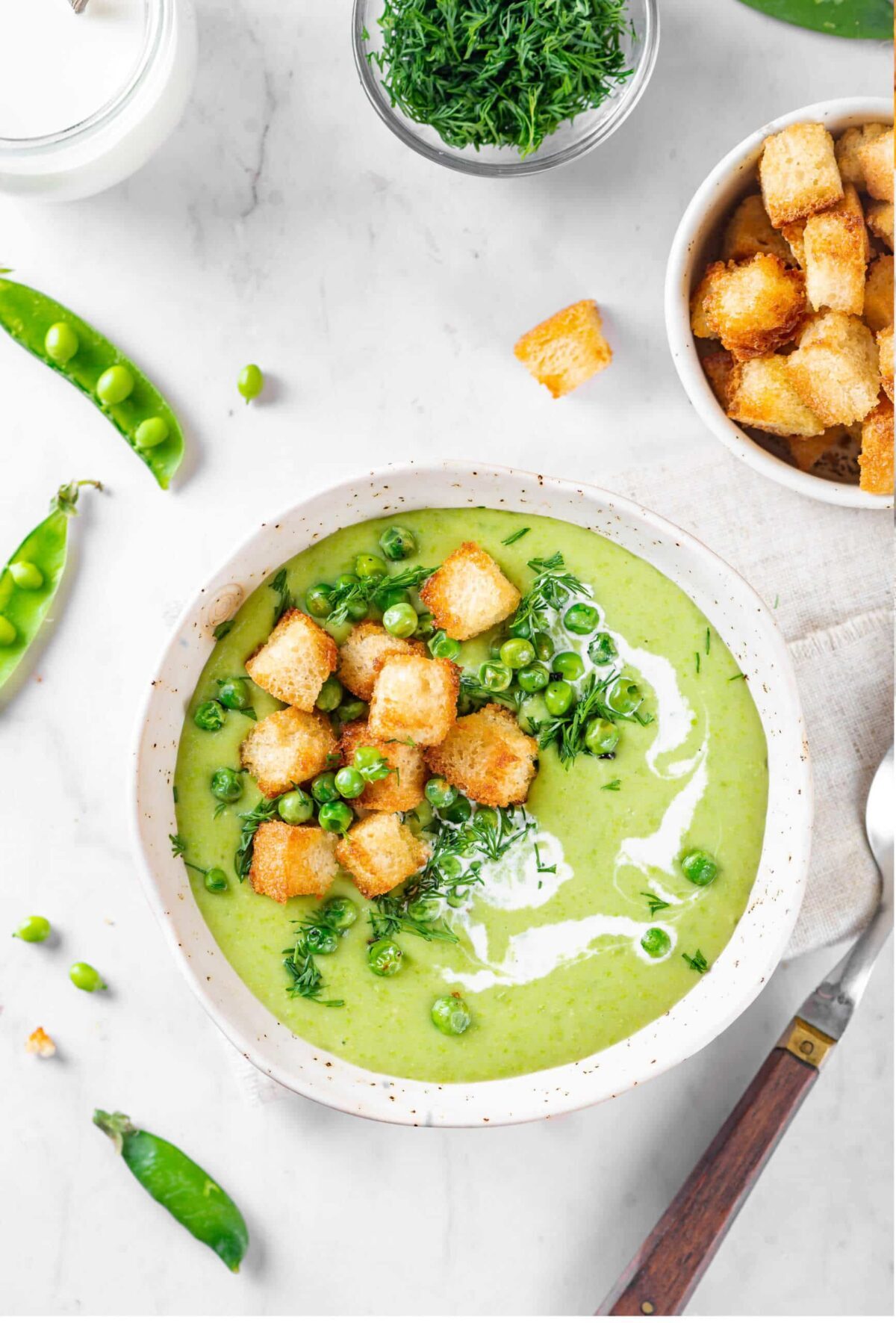 a bowl of pea soup with croutons on top and peas and a separate bowl of corutons on the side.