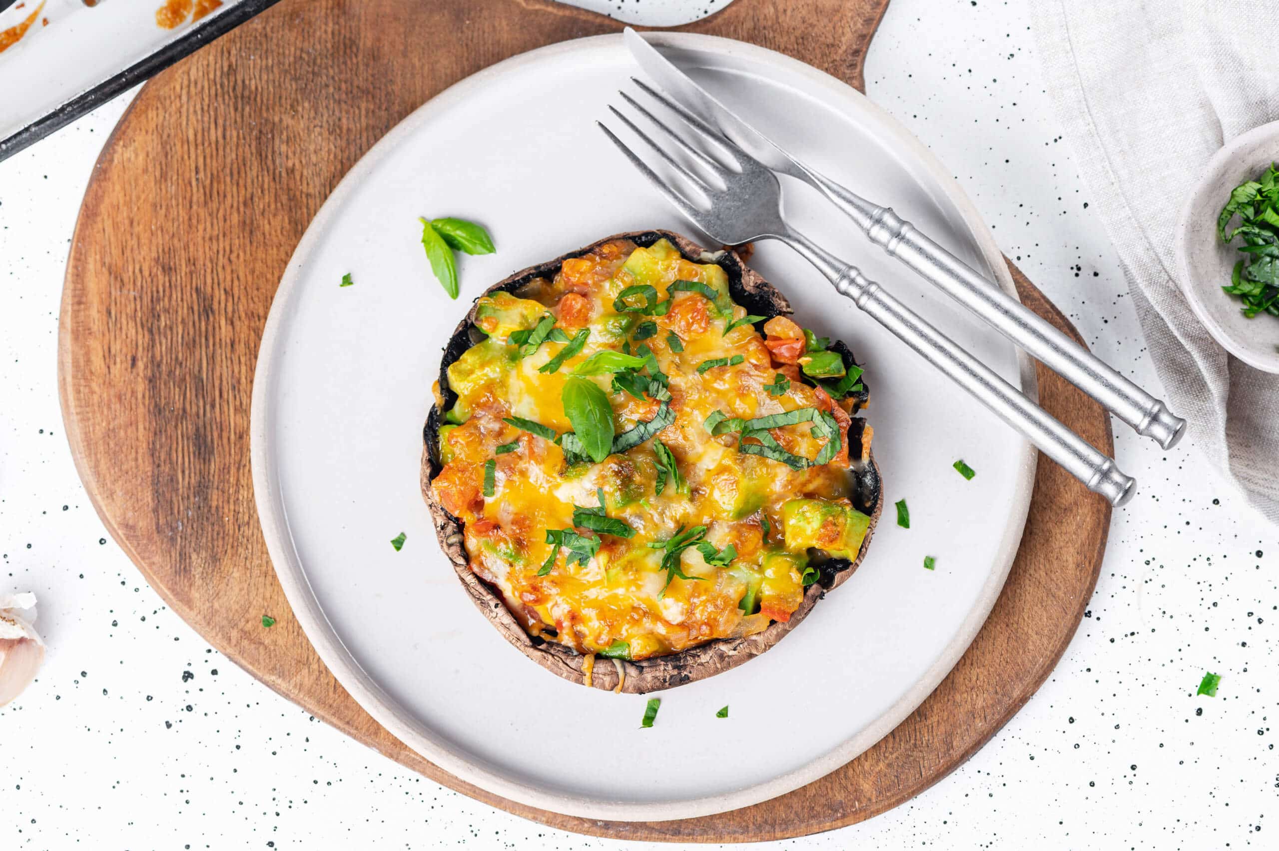 mushroom pizza sliced on a white plate with a knife and fork on a wooden board.