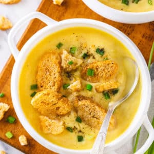 top view of a bowl of creamy cauliflower soup with croutons on top and chopped green onions sprinkled and a spoon.