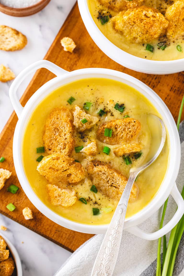 top view of a bowl of creamy cauliflower soup with croutons on top and chopped green onions sprinkled and a spoon.