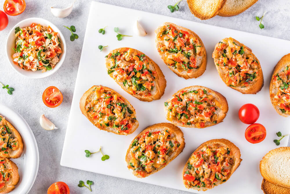 Bruschetta on a white cutting board with some ingredients around.