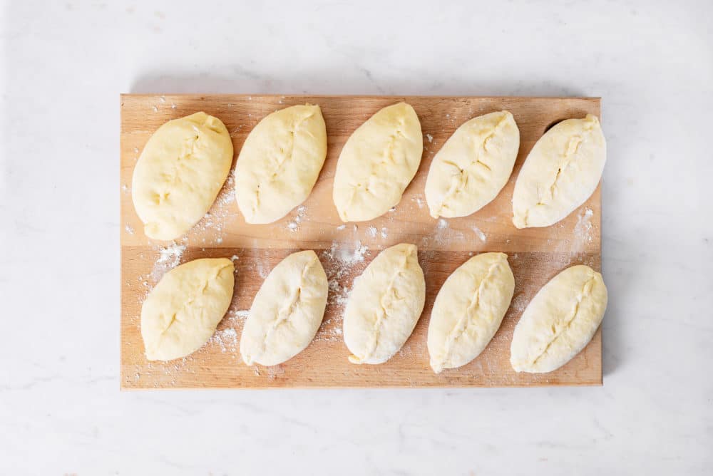 Raw piroshki filled with mashed potato on a wooden cutting board.