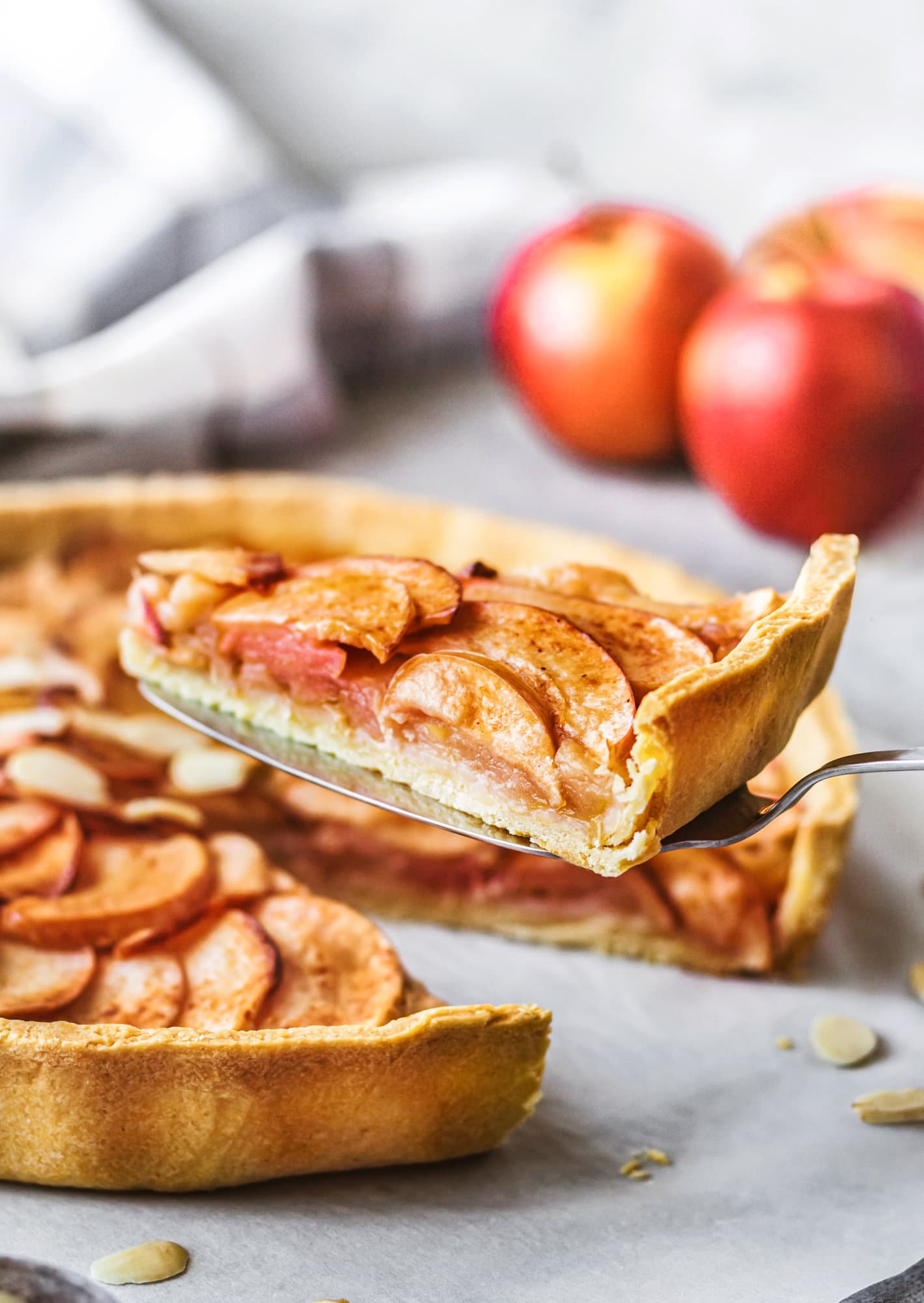 Apple tart slice picked up with a fork and apples in the background. 