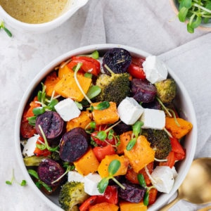 roasted veggies in a white dish with feta cheese cubes and microgreens sprinkled on top.