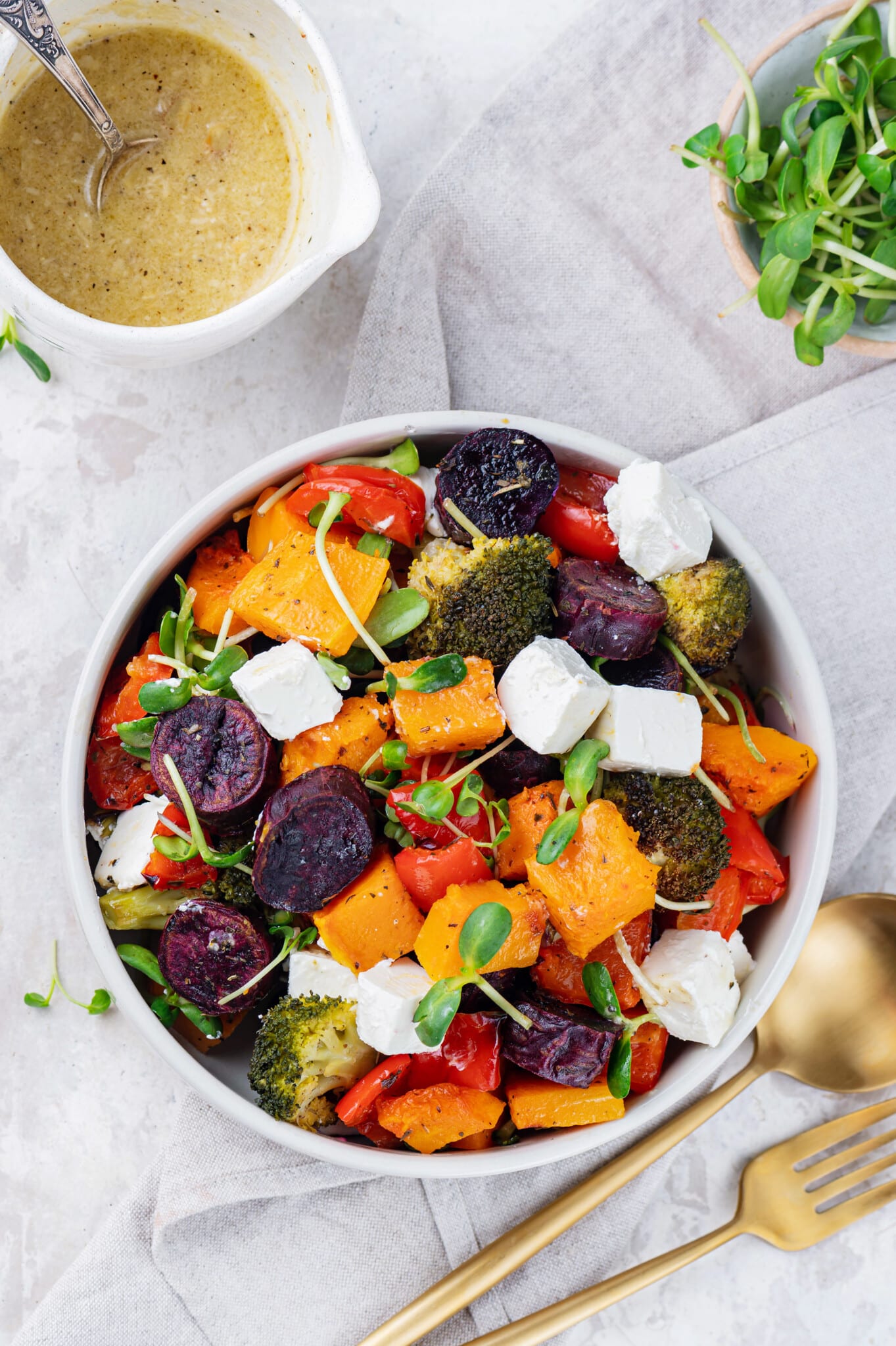 roasted veggies in a white dish with feta cheese cubes and microgreens sprinkled on top.